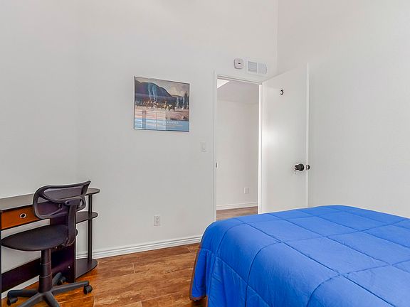 Bedroom has high ceilings bright and light room with desk and chair and mini fridge.