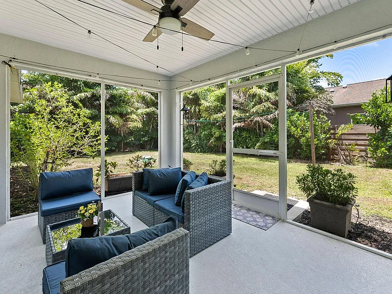 Screened-in covered patio with seating area, ceiling fan, and string lighting, opening to a private backyard.