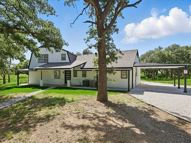 View of front of home with gravel driveway, an attached carport, roof with shingles, and central AC unit