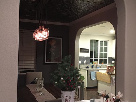 View from the living room into the dining room and kitchen. Dining room has a decorative tin ceiling and dimmable light fixture