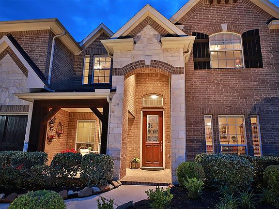 STONE AND BRICK ELEVATION WITH WOOD SHUTTERS - Embellished by a decorative Austin Stone entrance, this home exudes class. The front patio to the left is private with outlining hedges. Beautiful Mahogany 8' door with Designer Glass insert and brick pa
