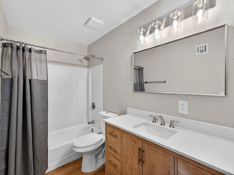 Clean full bath with tub/shower combo, wide vanity countertop, and large wall mirror with updated lighting.