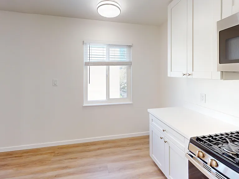 Bright and modern kitchen with sleek white cabinetry, stainless steel appliances, and warm wood flooring bathed in natural light from a sunny window. Bright and modern kitchen with sleek white cabinetry, stainless steel appliances, and warm wood flooring 
