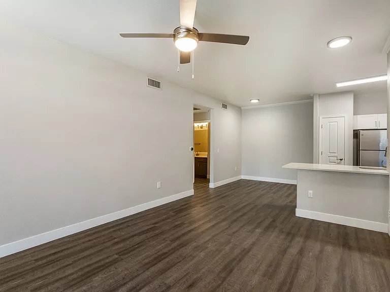 An airy living room beckons with a tranquil ceiling fan, while the kitchen beyond hints at culinary adventures