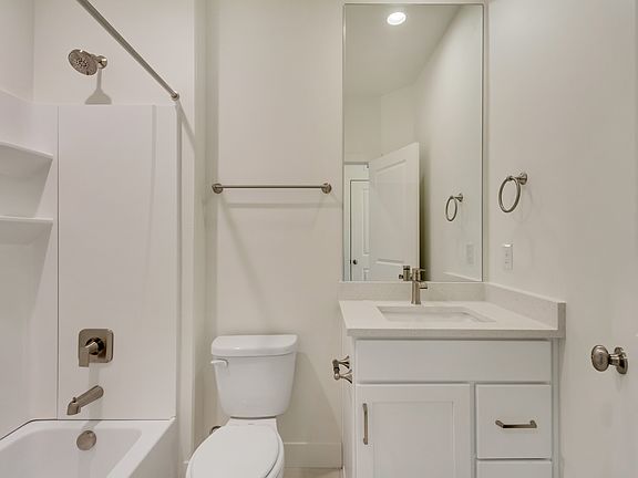 Modern bathroom with a white bathtub and shower, a toilet, a white vanity with a sink, a large mirro