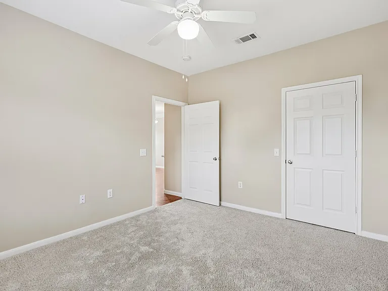 Inviting bedroom with plush carpeting, neutral walls, and white ceiling fan, offering a cozy and bright atmosphere. Inviting bedroom with plush carpeting, neutral walls, and white ceiling fan, offering a cozy and bright atmosphere.