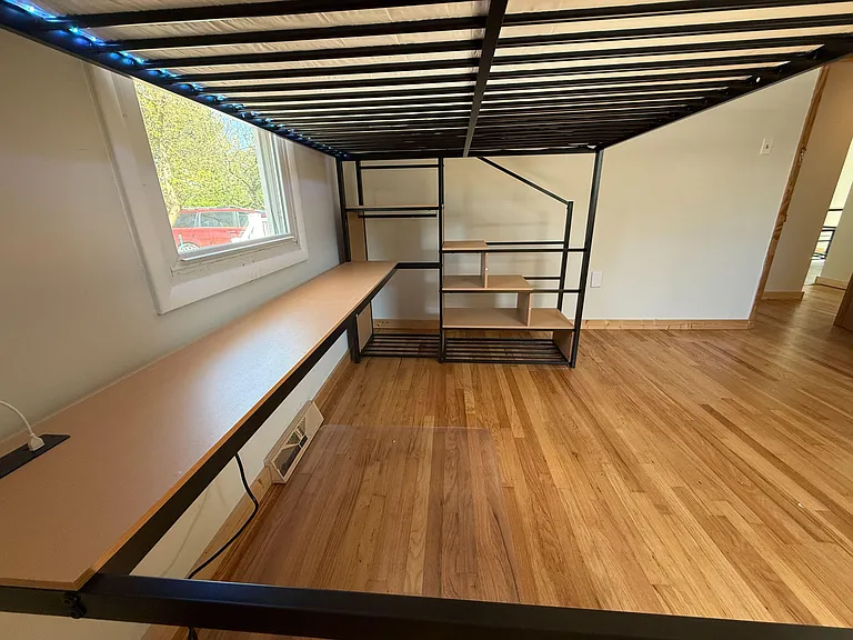 Bedroom features a loft-style bed frame with built-in shelving and a long desk, plus a window and wood-look flooring.