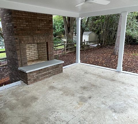 outdoor fireplace with covered porch in fenced backyard