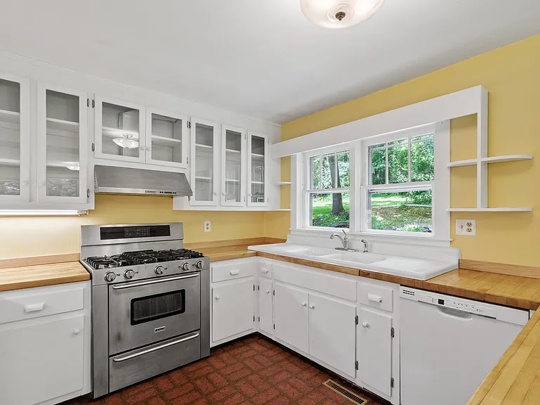 A spacious kitchen with newly refinished butcher block counters, glass front cabinets, original farm house sink and a view of the stream and herb garden.