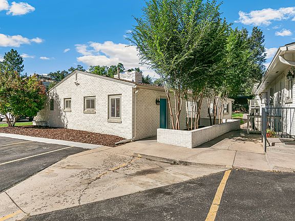 Charming brick apartment with lush greenery, featuring a spacious walkway and inviting exterior in a serene neighborhood.