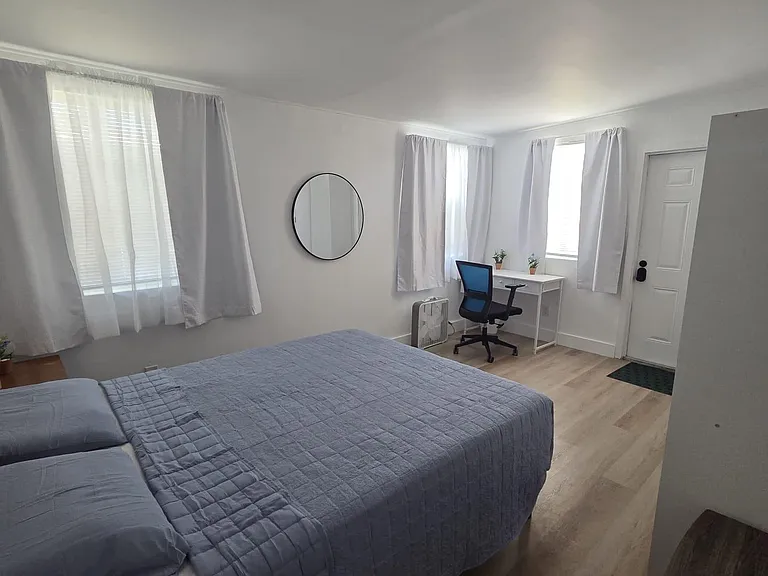 Spacious bedroom with multiple windows, a queen bed, and a dedicated desk areaideal for work-from-home setup.