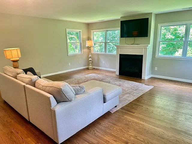 Large sunny living room with gas fireplace and a door that leads to a large outdoor deck.