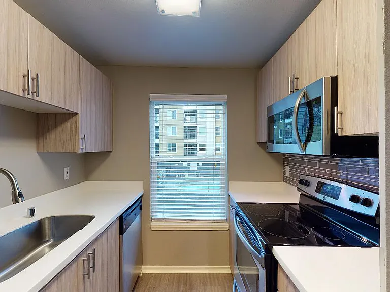Apartment kitchen with stainless steel appliances, quartz countertops and wood-style flooring.