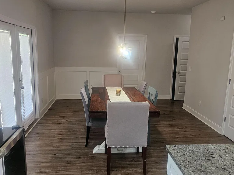 Dining area with a full-size table under pendant lighting, wainscoting detail, and sliding doors for outdoor access.