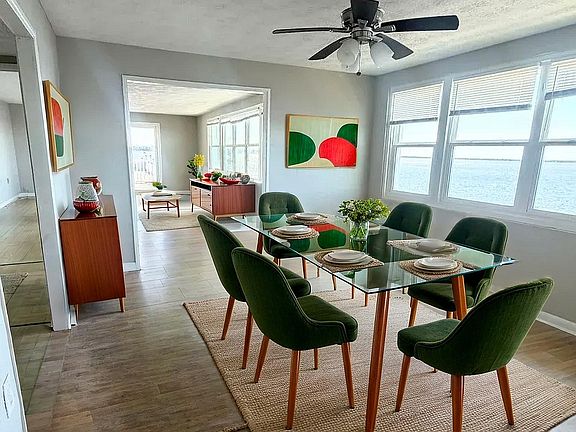 Chic dining area with green velvet chairs and glass table, showcasing modern decor and abundant natural light with stunning ocean views.