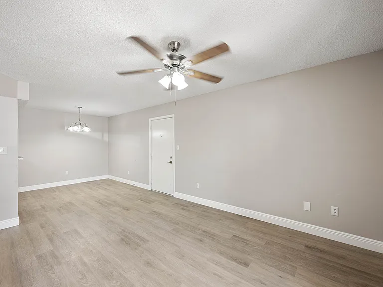 Bright open-concept living area with elegant ceiling fan and modern light fixture, featuring stylish wood flooring and neutral wall tones.