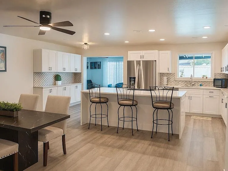 Open kitchen with large island seating, ample white cabinetry, stainless fridge, and adjacent dining area.