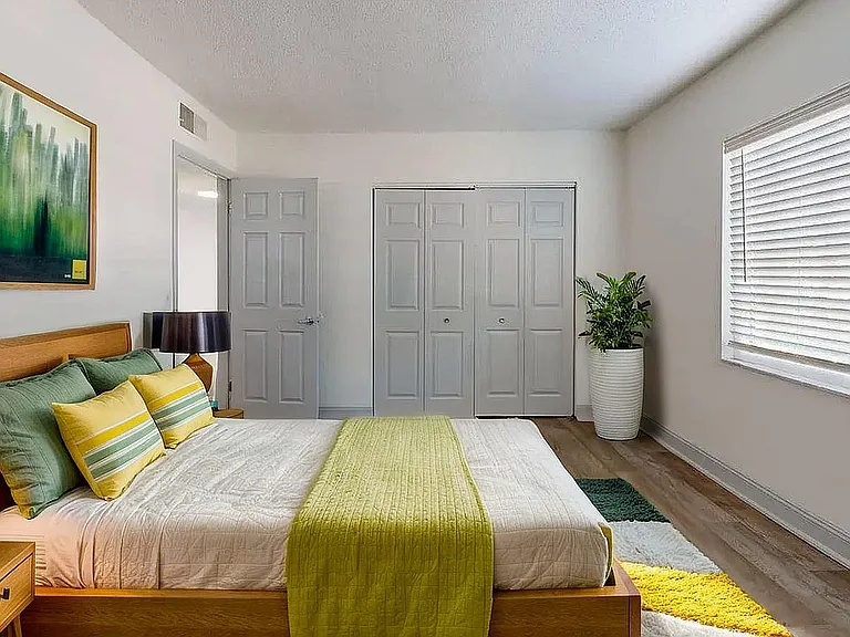 Bright and inviting bedroom with modern decor, featuring a plush bed, stylish artwork, and ample natural light from large window blinds.