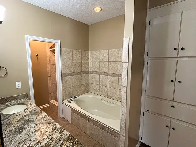 Master bathroom with large built-in storage cabinets, granite counter, and garden tub