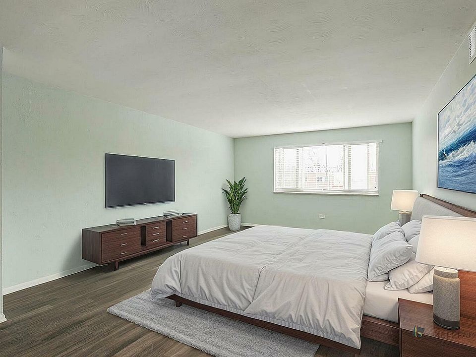 Inviting bedroom with soft green walls, featuring a cozy bed, modern wooden furniture, and a large window letting in natural light.