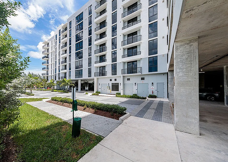 Tides at River Rapids apartments building exterior with modern architecture, lush greenery, and spacious pathway.