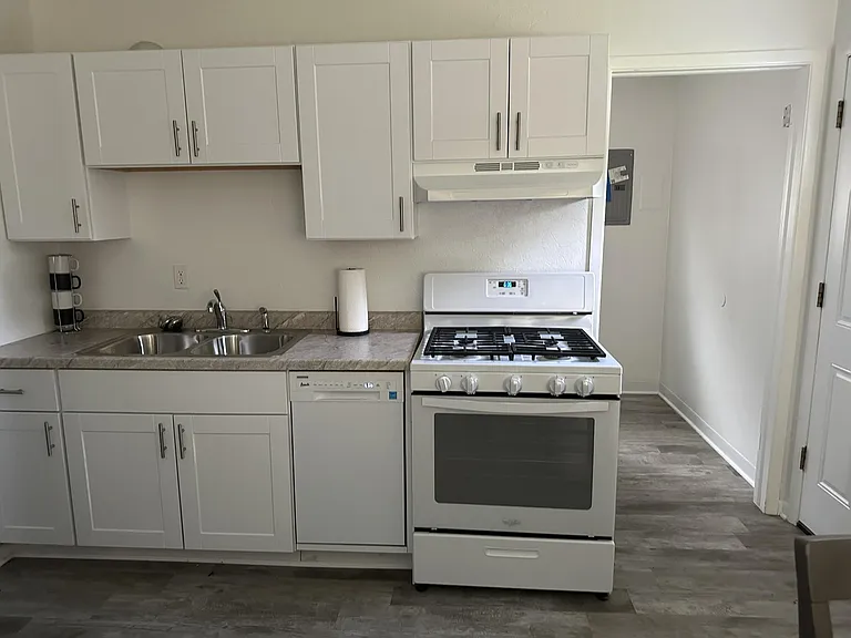 Efficient kitchen with ample white cabinetry, double-basin sink, dishwasher, and full-size range with vent hood.