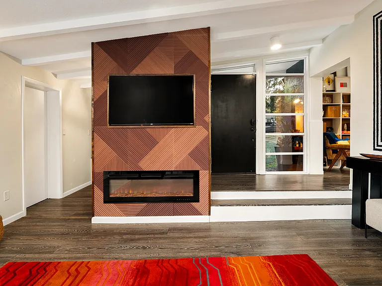 "Sunken Sitting Room" off the home's entry has a remote controlled fireplace and a TV. The room also has bookshelves and console table with stools for additional seating.