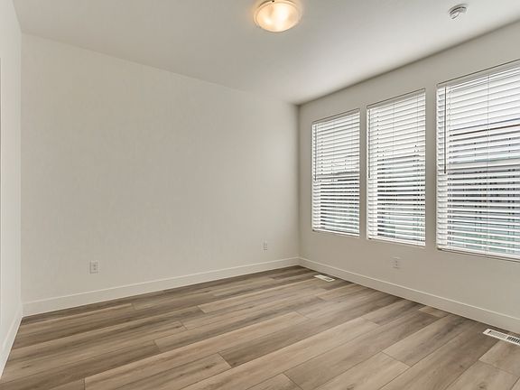 Empty room with wooden floors, white walls, and three large windows with blinds. Ceiling light fixtu