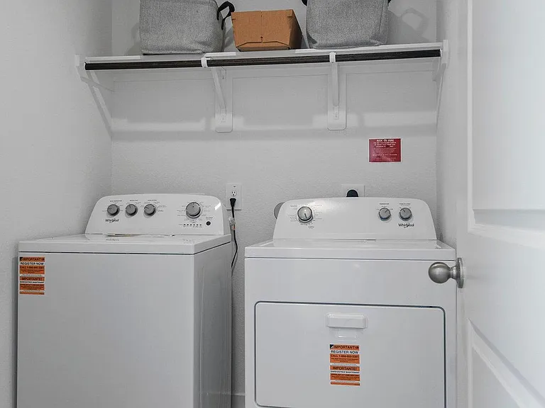 Dedicated laundry closet with full-size washer and dryer plus an overhead shelf for supplies and added storage.
