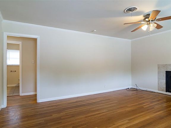 Living room with a wood burning fireplace.  The fireplace has a gas starter.   Original hardwood floors and a ceiling fan.