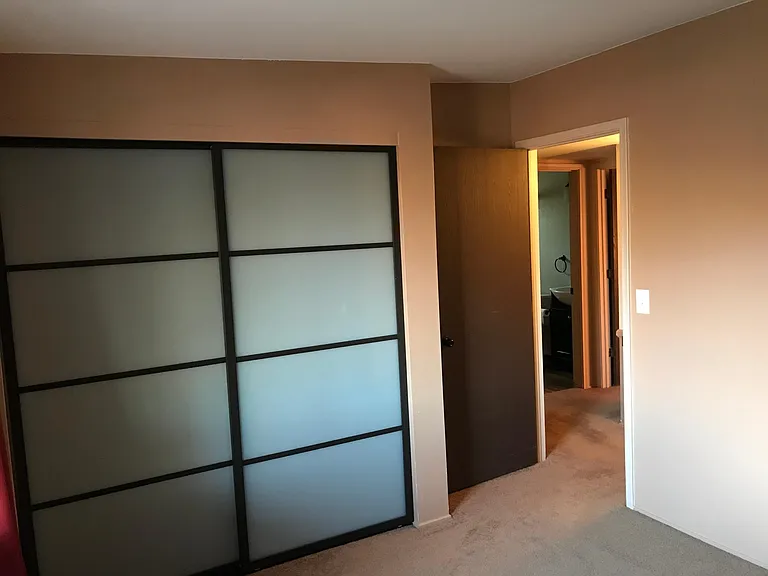 Bedroom 2 with frosted glass doors and adjacent to the second 3/4 bath and storage closet in the hall.