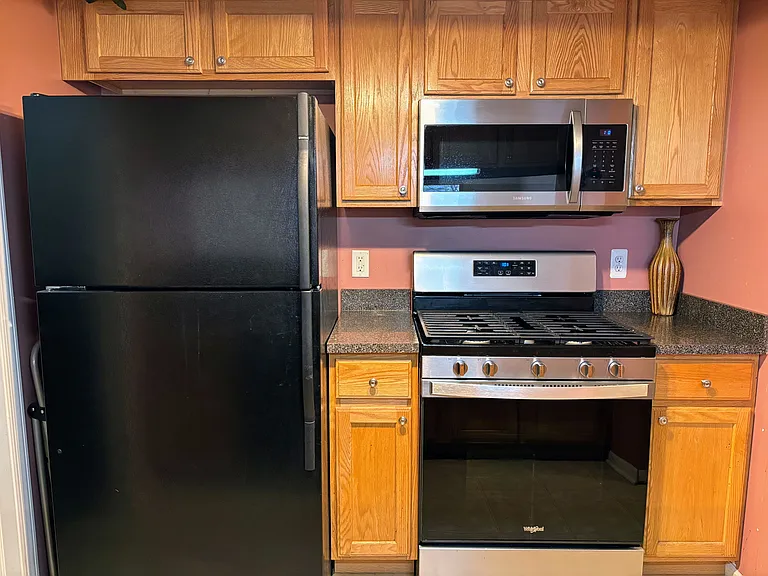 Kitchen with newer stainless steel and black appliances. More cabinets on the other side.