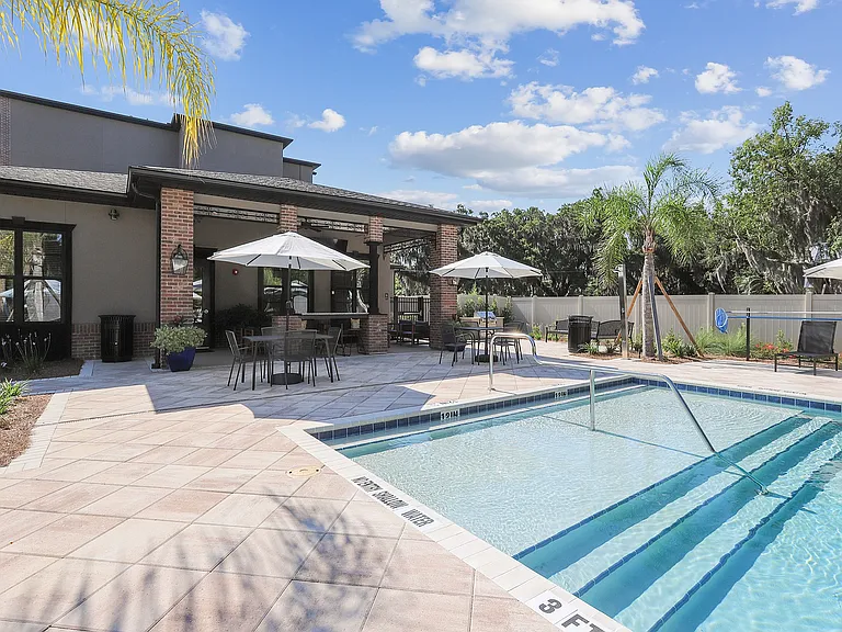 Inviting outdoor space featuring a sparkling pool, shaded seating area with umbrellas, and lush greenery, ideal for relaxation and entertainment.