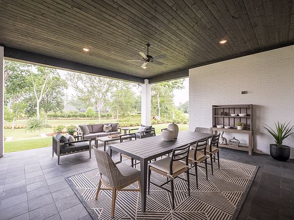 A covered outdoor patio with a dining table and chairs, surrounded by lush greenery and trees visibl