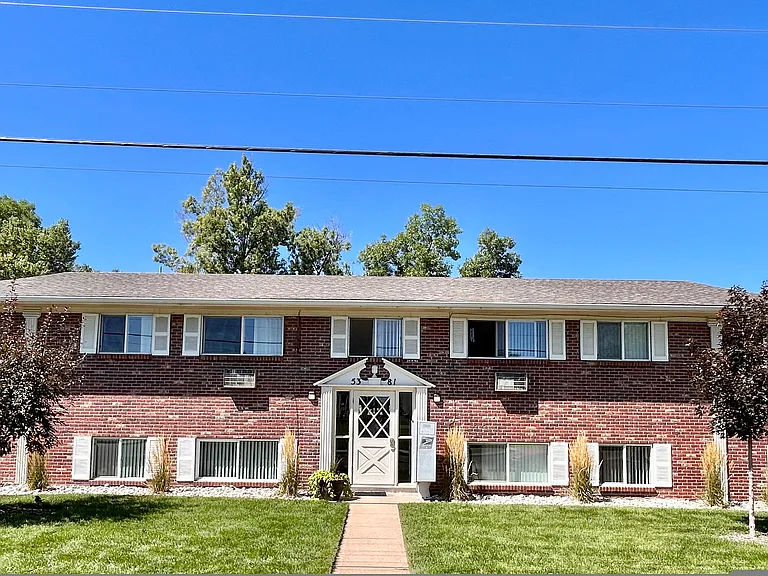 Brick apartment building with a well-maintained lawn, featuring a symmetrical design and multiple windows.
