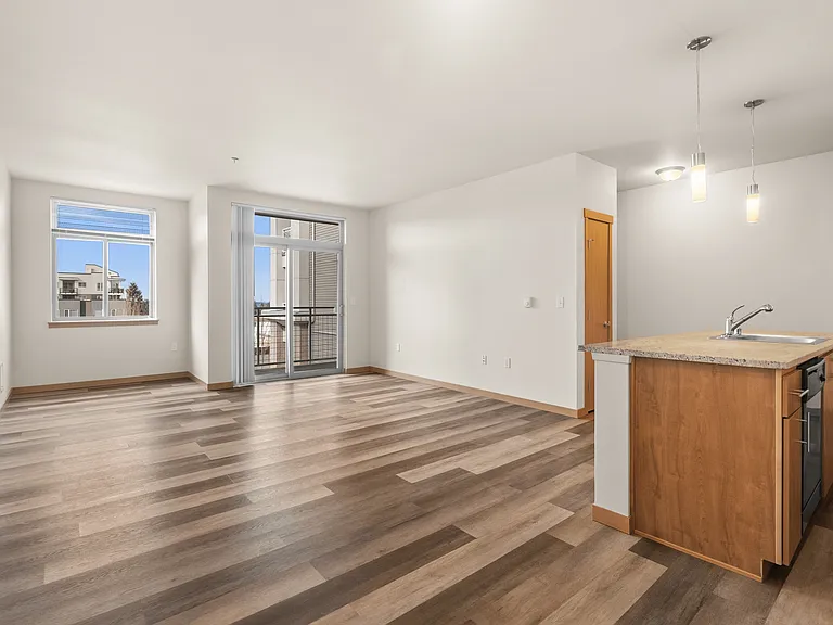 Bright open-concept living area with wood-style flooring and modern kitchen island, featuring large windows and ample natural light. Bright open-concept living area with wood-style flooring and modern kitchen island, featuring large windows and ample natu