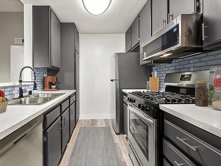 Blue tiled kitchen with stainless steel microwave, oven, and refrigerator.