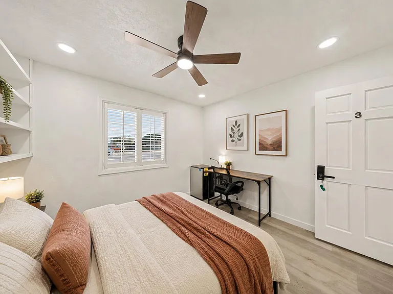 Well-appointed bedroom with built-in shelving, ceiling fan, and a dedicated desk area plus mini fridge for added convenience.