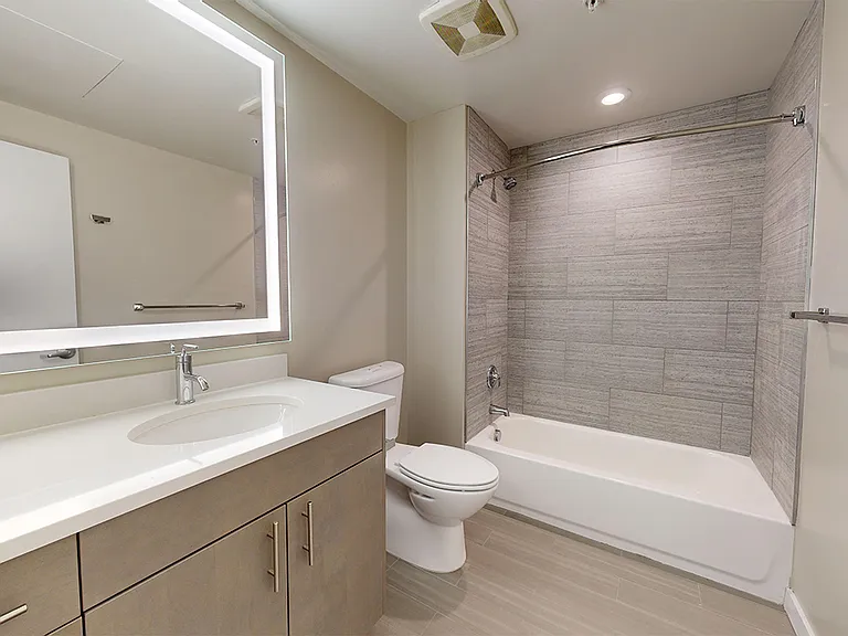 Apartment bathroom with wood-style flooring and LED vanity mirror.