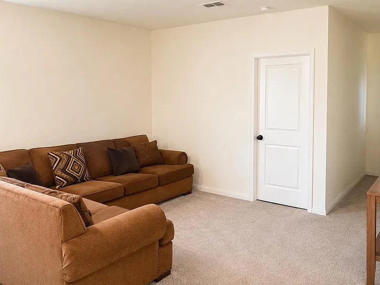 Spacious living room with a sectional seating area, neutral walls, soft carpeting, and easy access to the entry/hallway.