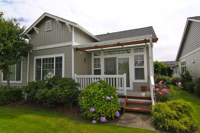 Back Side of Home with covered deck and views to the park area. Beautiful trees, shrubs and flowers.