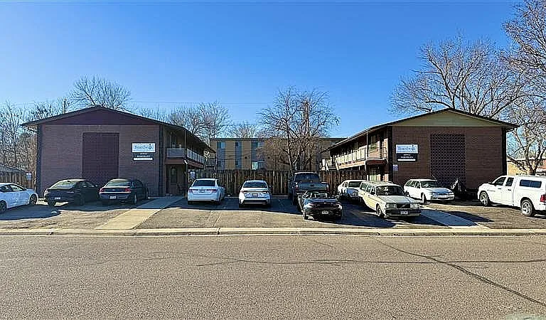 Charming brick apartment complex with ample parking, surrounded by trees for a serene living environment.