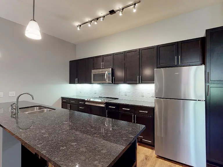 Apartment kitchen with stainless steel appliances, granite countertops and wood-style flooring.