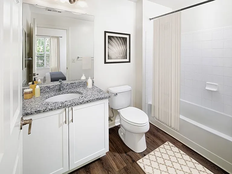 Phase I Renovated Package I apartment bath with grey speckled granite countertop, white cabinetry, and hard surface flooring