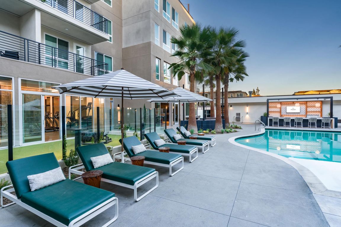 Relax by the resort-style pool at Modera Pomona, featuring a lounge area, seating, and palm trees.