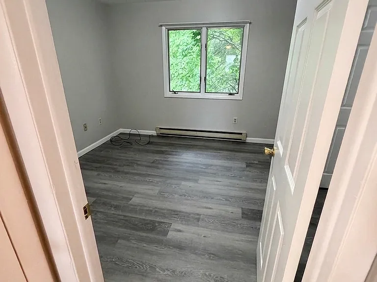 Welcoming bedroom space with a large window letting in natural light, complete with freshly painted neutral walls, updated baseboards, and newly installed LVP flooring.