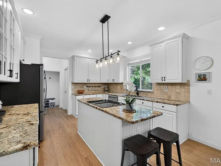 Kitchen featuring an island with beadboard paneling, recessed lighting, wood-finish flooring, a tile backsplash, and white cabinetry with dark hardware
