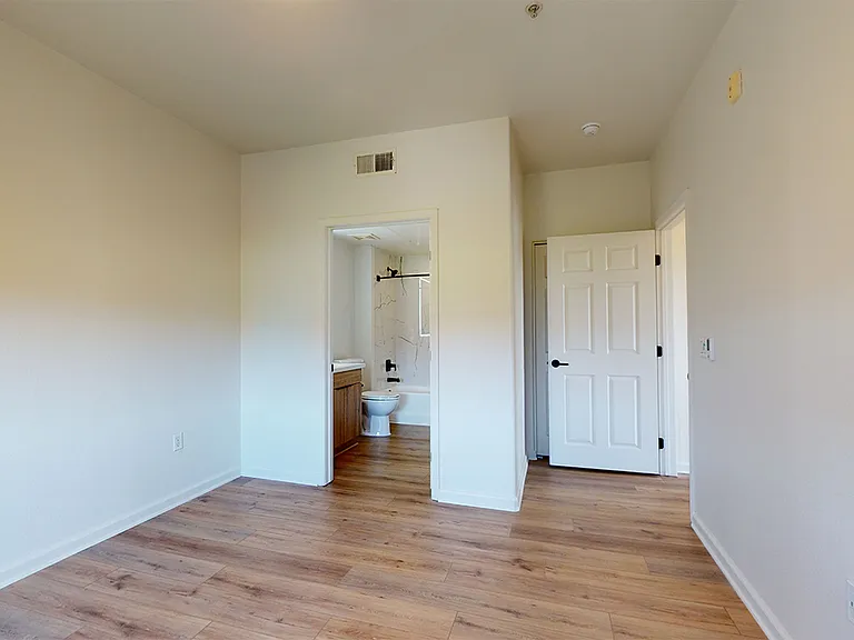 Spacious apartment bedroom with attached bathroom and wood-style flooring.