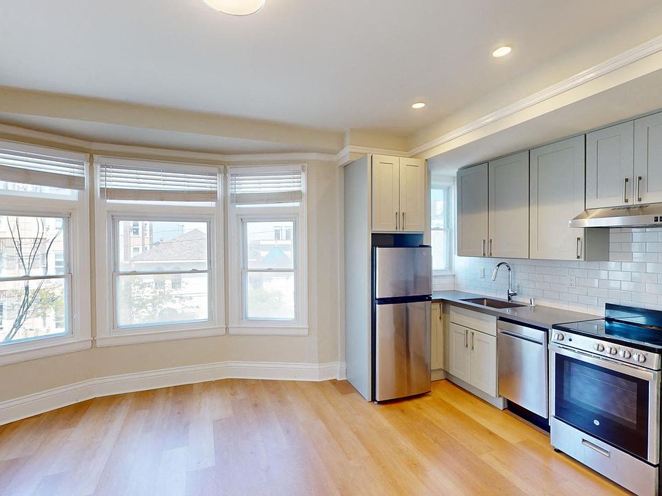 Living room with a large window, wood-like flooring, and a view of the kitchen