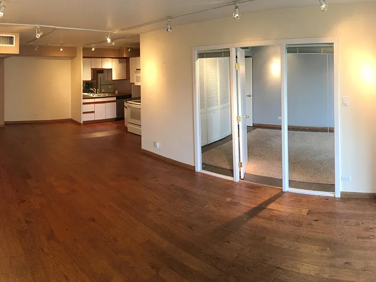 Standing near balcony door looking back into living room. Bedroom in background (right) with door and blinds.